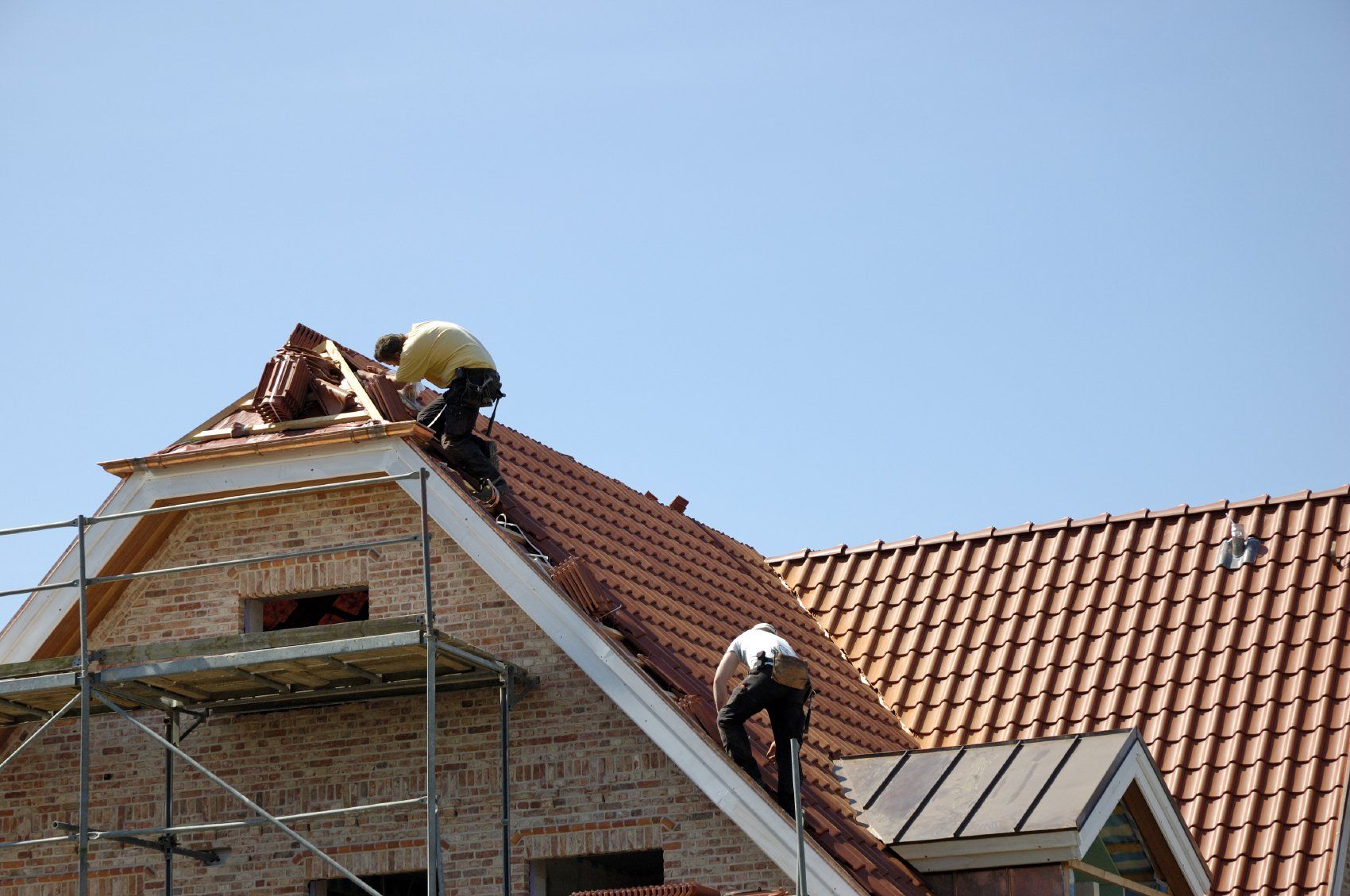 Handwerker auf einem Dach mit roten Ziegeln bei der Arbeit